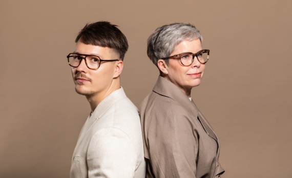 Mies ja nainen selät vastakkain. Molemmilla on silmälasit.